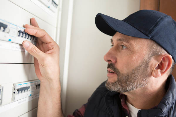 man resetting switch in circuit breaker cabinet due to outside air conditioner tripping breaker