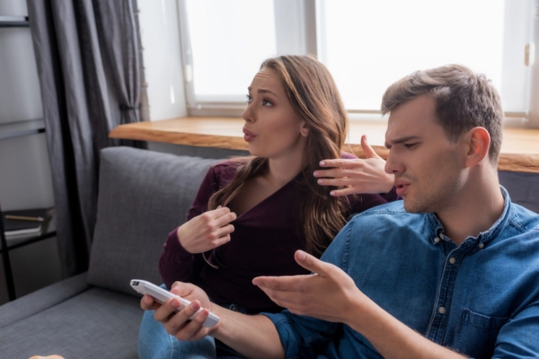 couple feeling warm while a guy looks at the air conditioner remote depicting HVAC efficiency