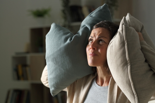 woman covering both ears with pillows depicting noisy window air conditioner