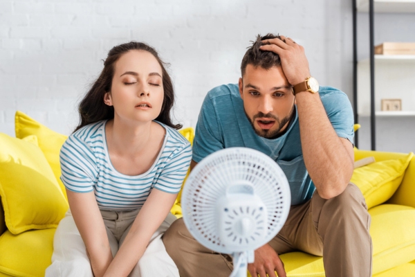couple sitting in front of electric fan in the living room due to AC not keeping up