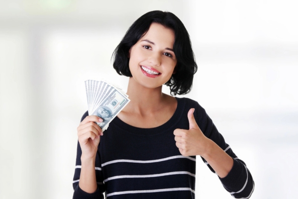woman holding dollar bills and gesturing a thumbs up sign on the other hand depicting Heating Oil Affordability and Value