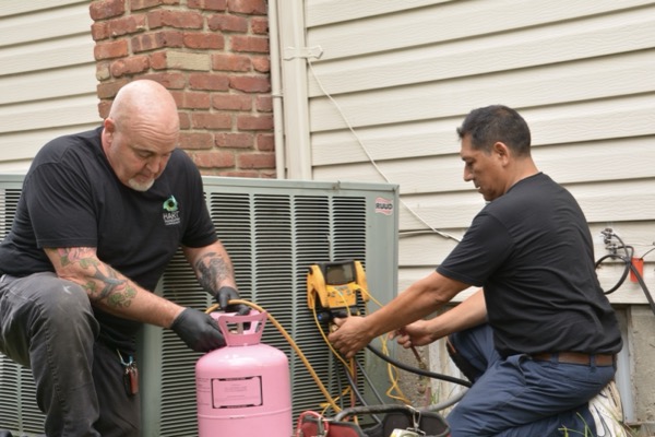 Babylon, NY technicians servicing central air conditioning unit with propane tank and tools