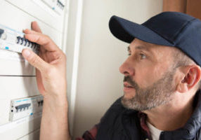 man resetting switch in circuit breaker cabinet due to outside air conditioner tripping breaker